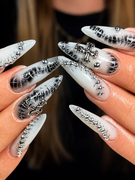 Ongles stiletto blancs avec croix gothique argentée et perles métalliques